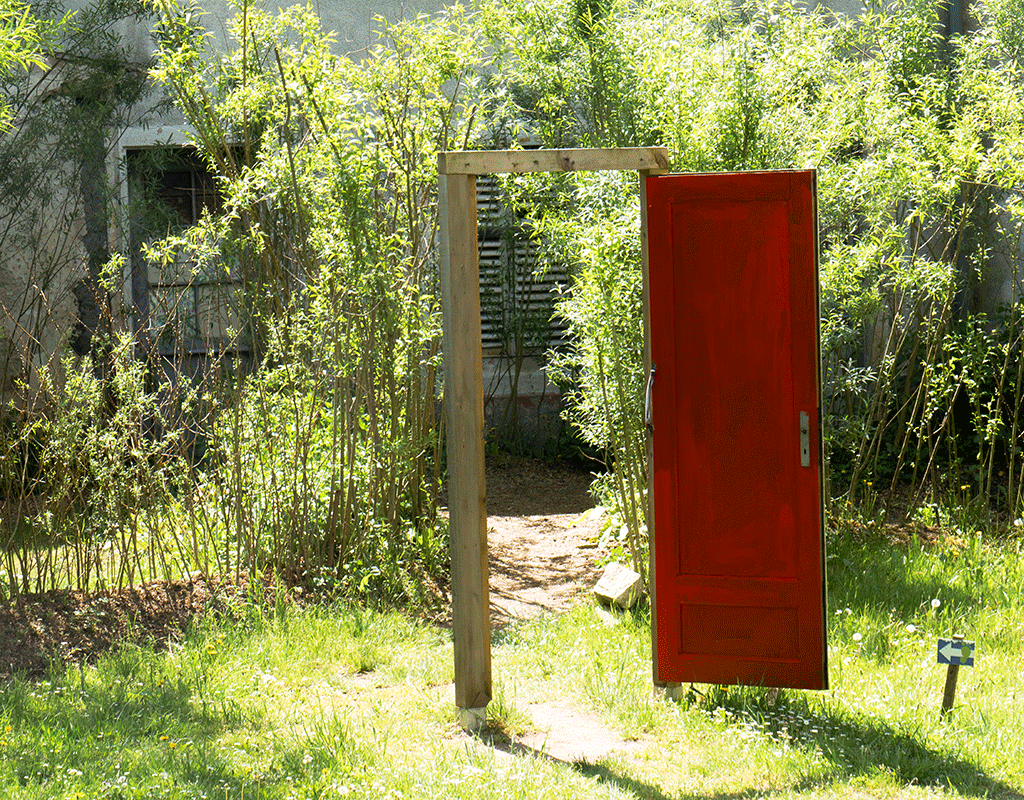 Foto: Gudrun Gempp, Parc de Wesserling, Mai 2015. Eine rote Tür, offen, in einem Rahmen, der im Parc de Wesserling frei im Garten steht.