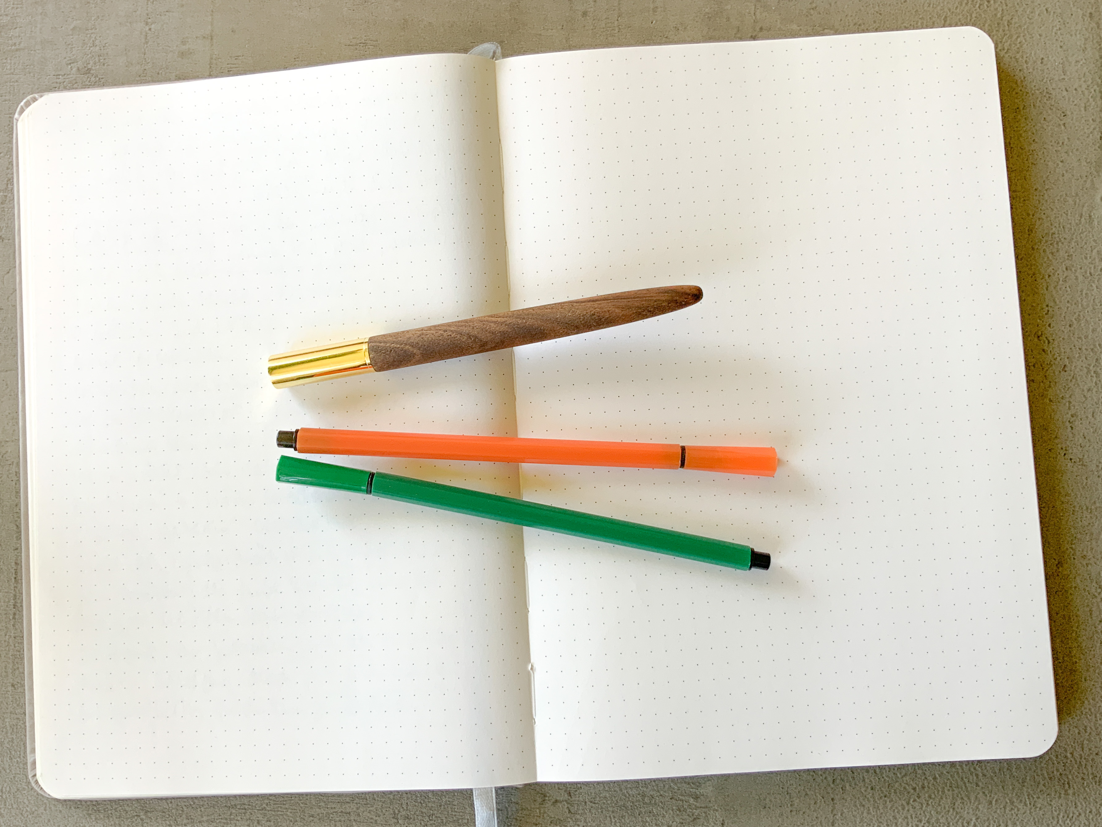 Ein aufgeschlagenes Notizbuch und drei Stifte.